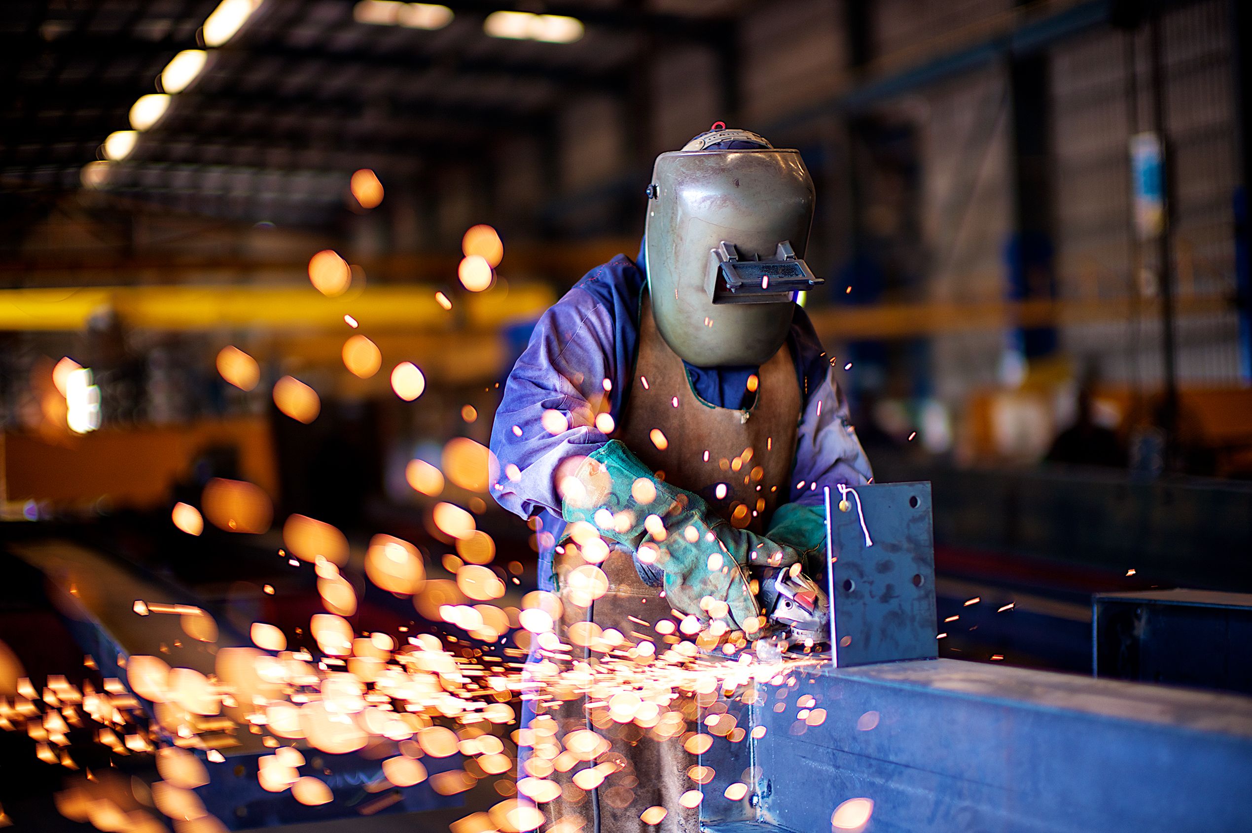 An industrial worker in a workshop welding metal with protective gear, creating vibrant sparks.